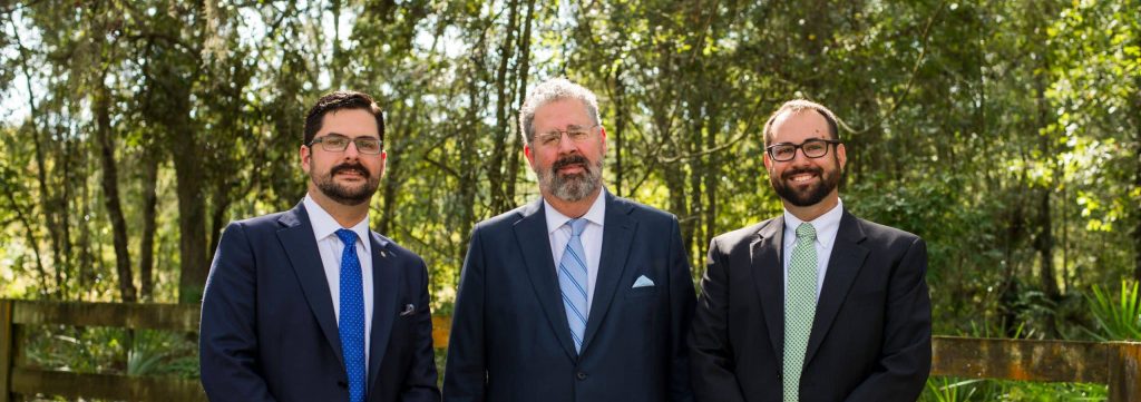 Murtha & Flischels partners professionally dressed, standing in front of a forest.